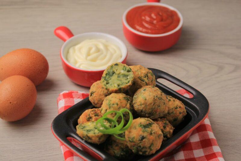 A red and black dish of balls next to two types of dip and some eggs