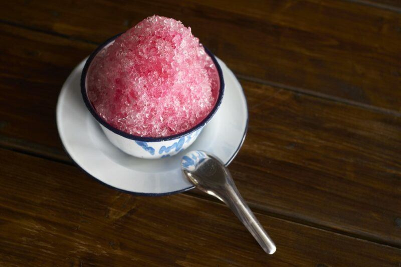 A small plate with a mug of frozen negroni snow cone, next to a spoon