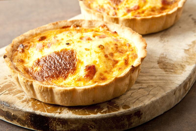 A small quiche lorraine on a board, with a second in the background