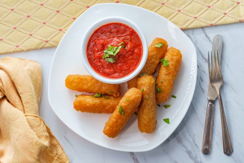 A white plate with vegan mozzarella sticks and a small bowl of dip