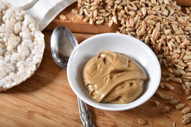 A white bowl of sesame seed butter with sesame seeds and a rice cake