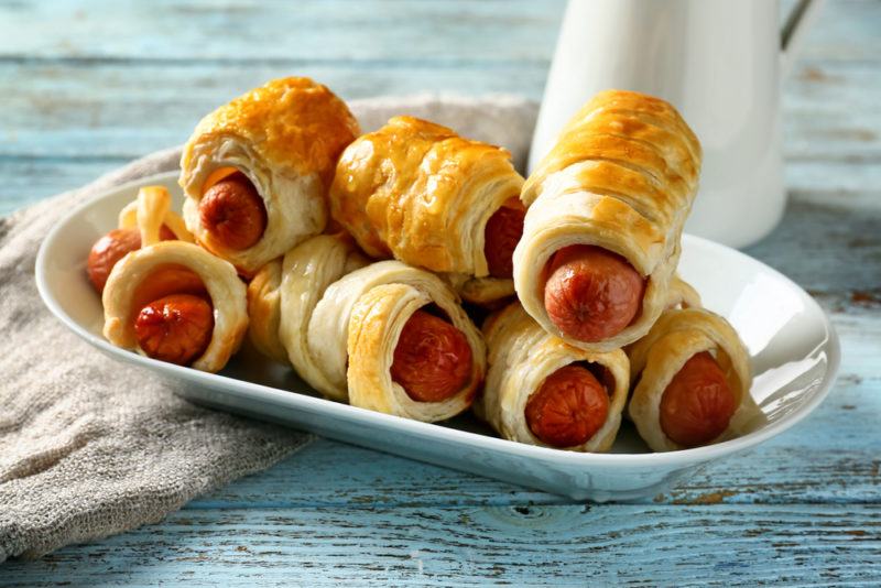 A white dish of pigs in a blanket on a blue-gray table