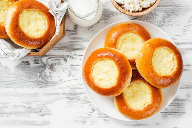 A white plate with small vatrushka treats on a white table, with a few more treats further away