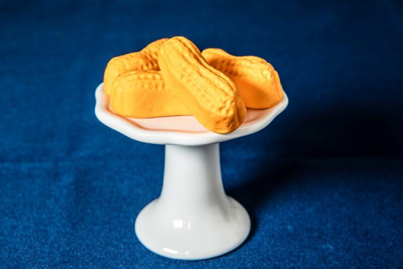 A small white stand containing a few candy circus peanuts against a blue cloth background