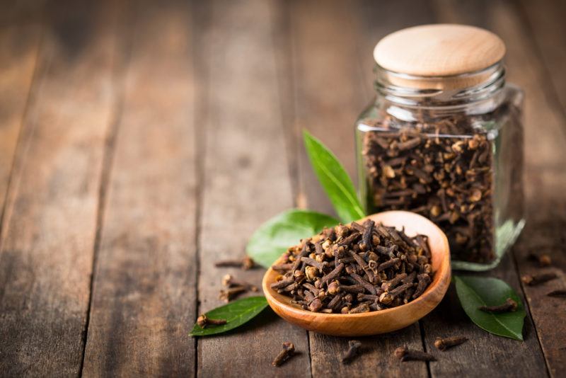 A small wooden bowl of cloves and a small jar that also contains cloves