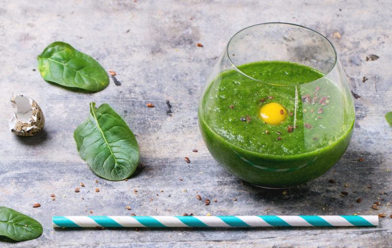 A green smoothie in a glass smoothie with an egg yolk