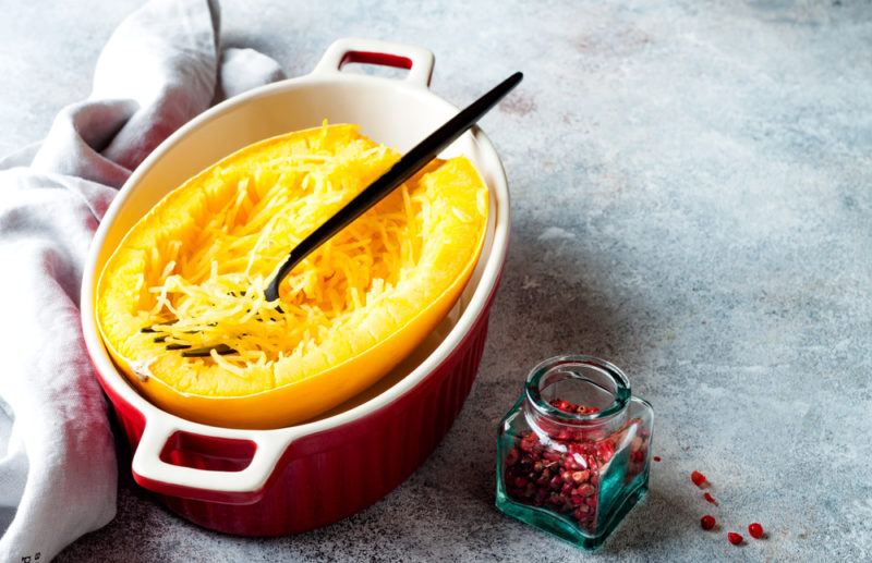 A red dish with a cooked spaghetti sqash and a spoon or fork