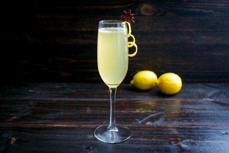 A champagne glass containing a spice 75 cocktail on a wooden table, with two lemons in the background