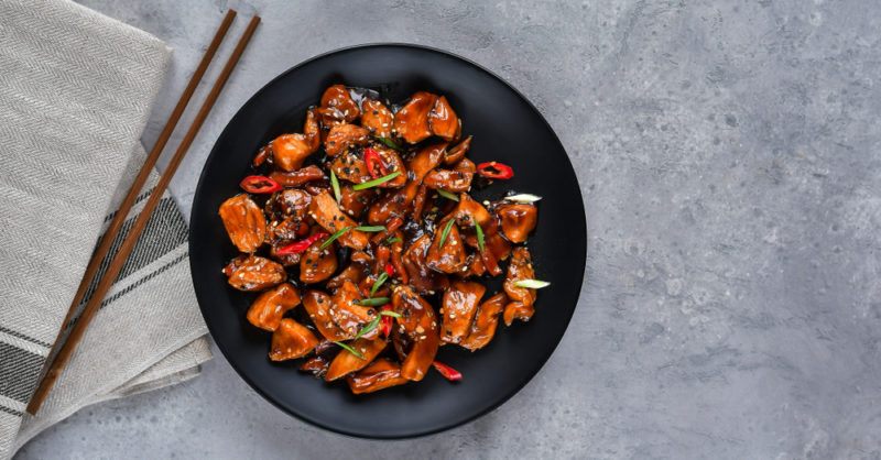 A black dish of spicy Asian chicken on a gray table