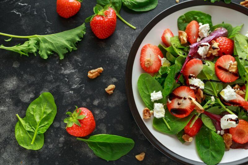 A black and white plate with a summer salad that includes spinach and strawberries