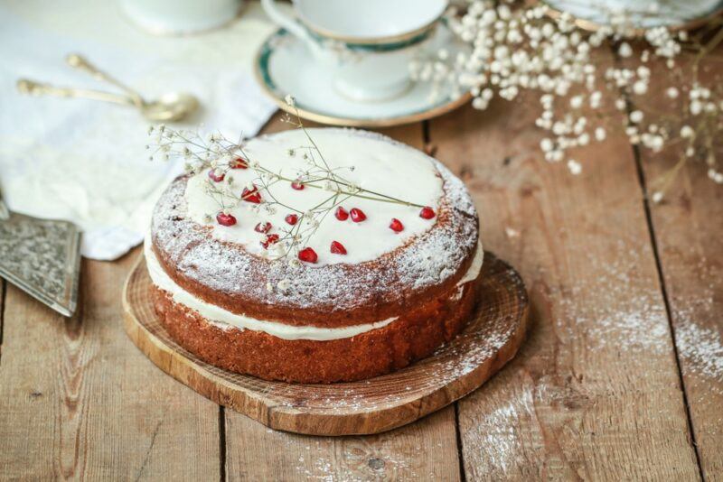 A wooden table with a sponge cake with white icing and pomegranate arils on the top