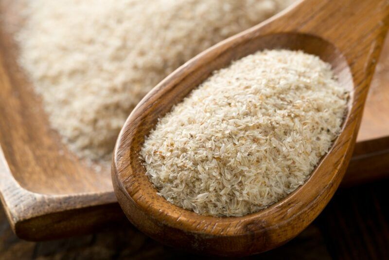 A large wooden bowl filled with psyllium husk powder, with a wooden spoon of the powder in the foreground