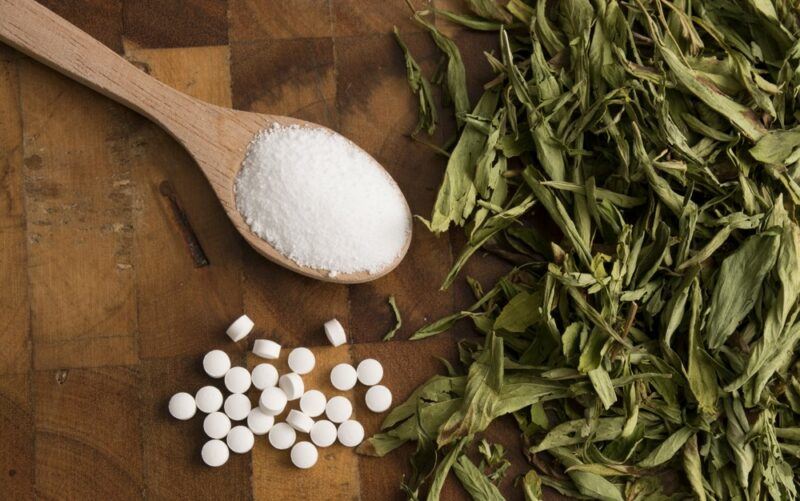 Dried stevia leaves, a spoon of stevia powder and stevia tablets