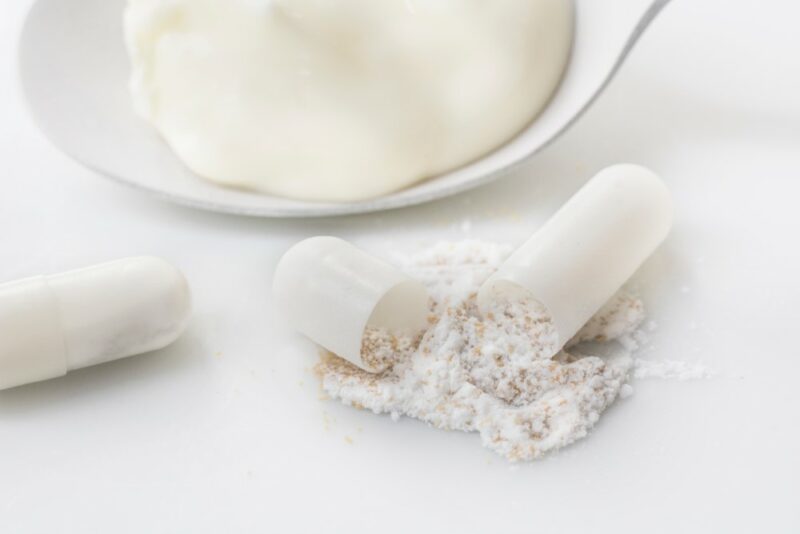 A white spoon of yogurt in front of two probiotic supplements, one of which has been opened