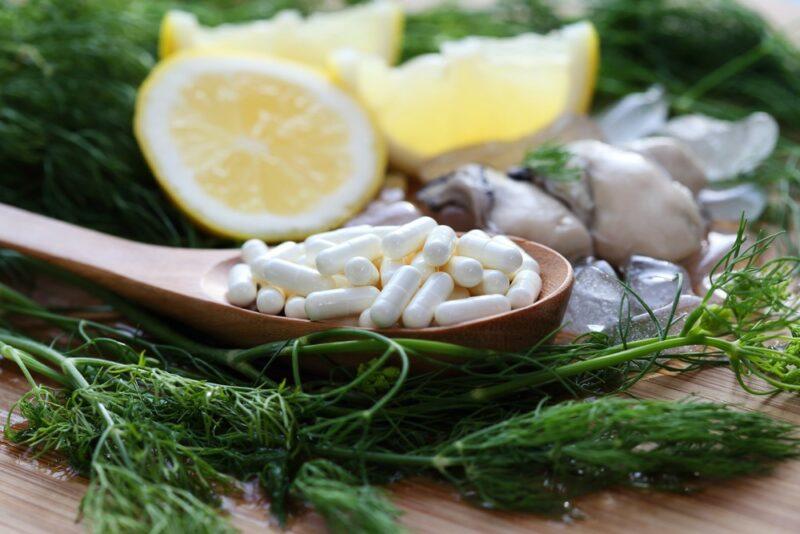 A wooden spoon containing zinc supplements, on top of some greens, in front of lemons and oysters