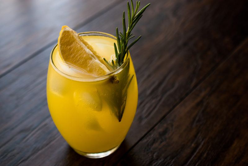 A glass of a citrus cocktail with a sprig of rosemary and a wedge of citrus fruit