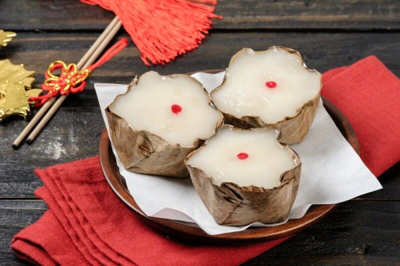 A plate with a white cloth and three pieces of nian gao. Each dessert is white with a spot of red in the center