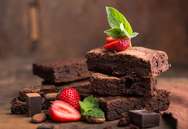 A stack of chocoalte brownies, with some strawberries and mint leaves