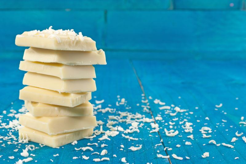 White chocolate in a stack against a blue background, with chocolate shavings