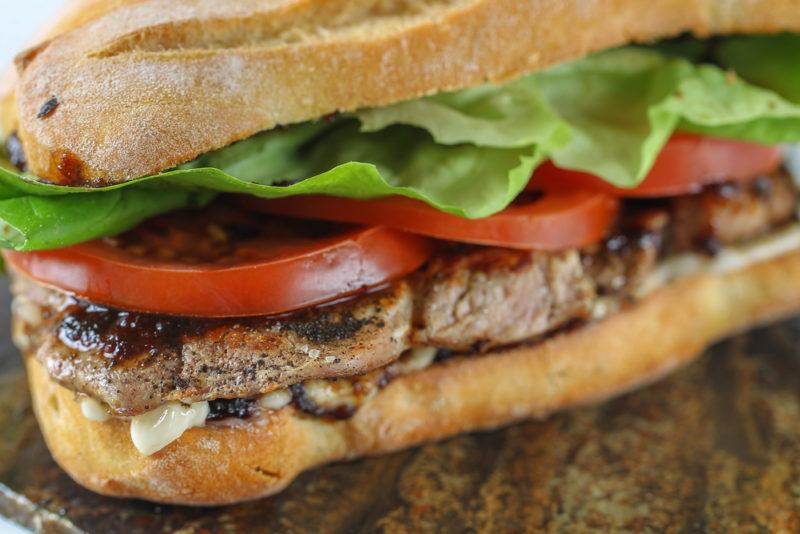 A large steak, lettuce and tomato sandwich on a wooden table