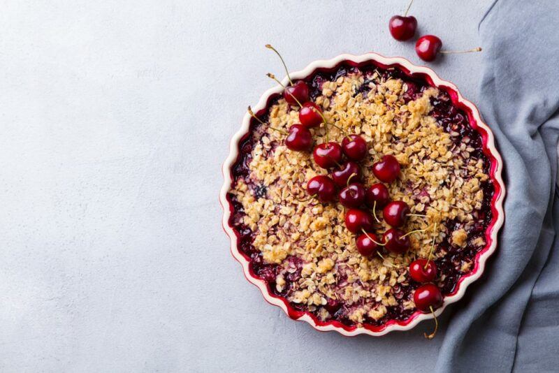 A pie dish filled with a strawberry and cherry pie with crumble on the top