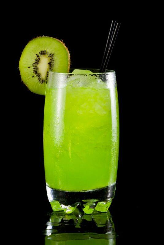 A single swamp frog cocktail on black, with a slice of kiwi as a garnish