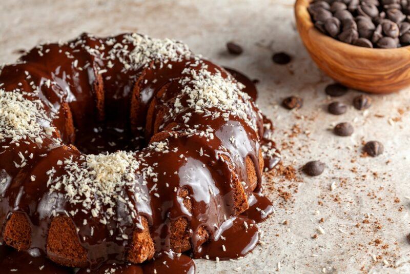 A gray table with a coconut and chocolate bundt cake, next to a dish of coffee beans and a few coffee beans on the table