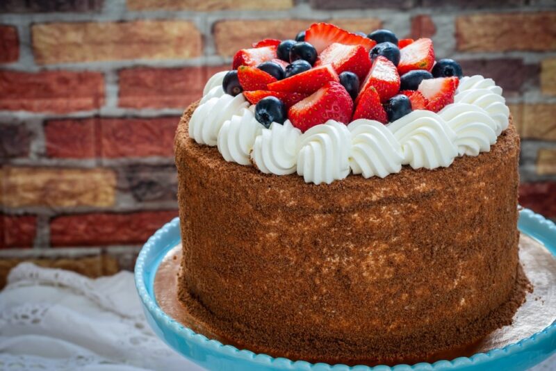 A blue plate with a tall Russian royal cake with icing, strawberries, and blueberries