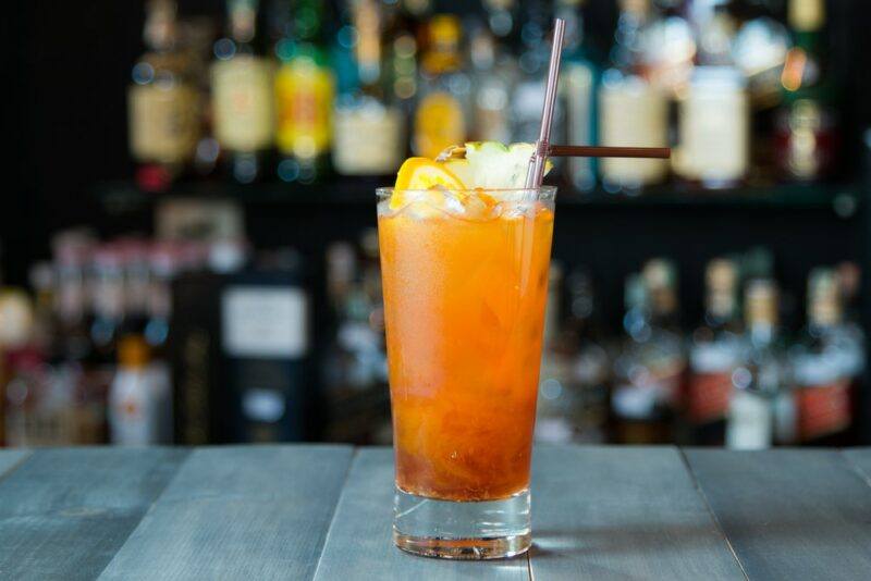 A tall glass containing a horsefeather cocktail in front of an out of focus bar