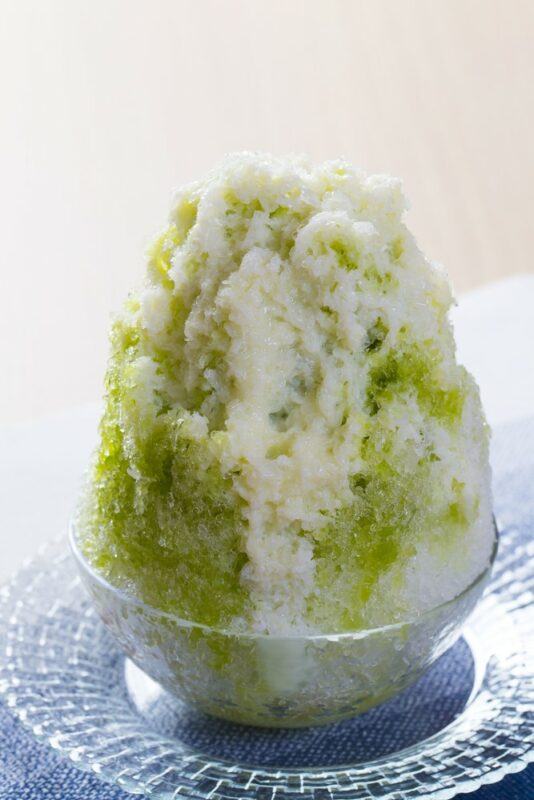 A glass dish on a plate, containing a tall pickle juice snow cone