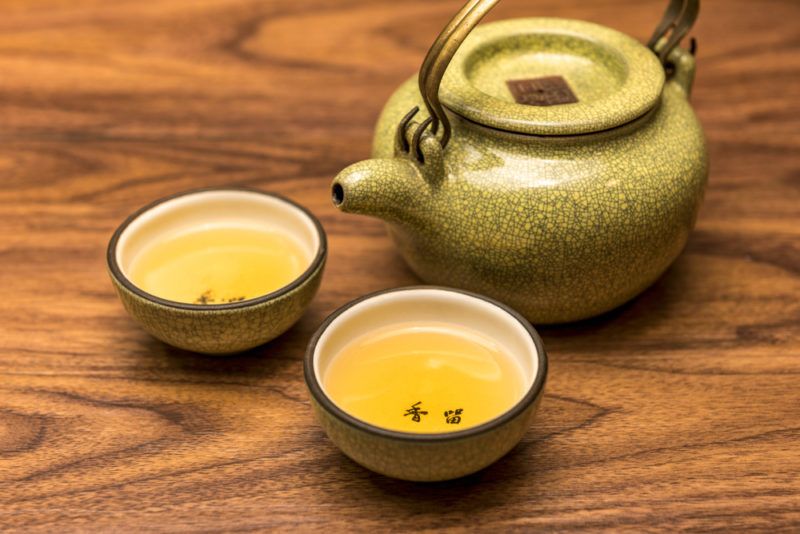 A green yellow teapot and two shallow cups that contain yellow tea