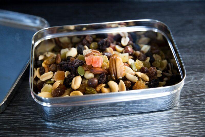 Some trail mix in a metal tin, including nuts, dried fruit, and chocolate