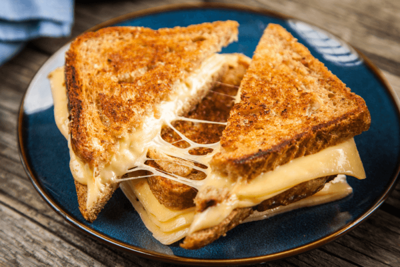 A blue plate with a toasted sandwich that has been cut in half, with plenty of stringy cheese.