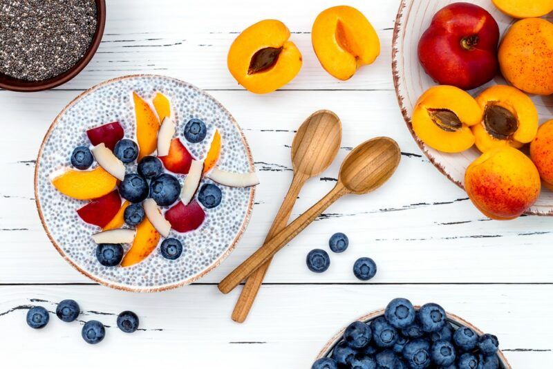 A white table with a chia seed pudding and a large selection of fresh fruit, including blueberries and apricots