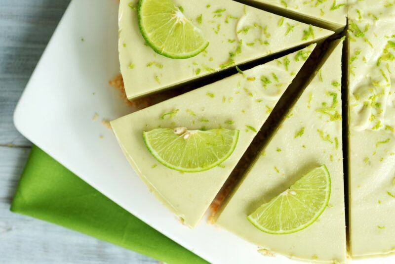 A white plate showing a large lime cheesecake with lime wedges on top