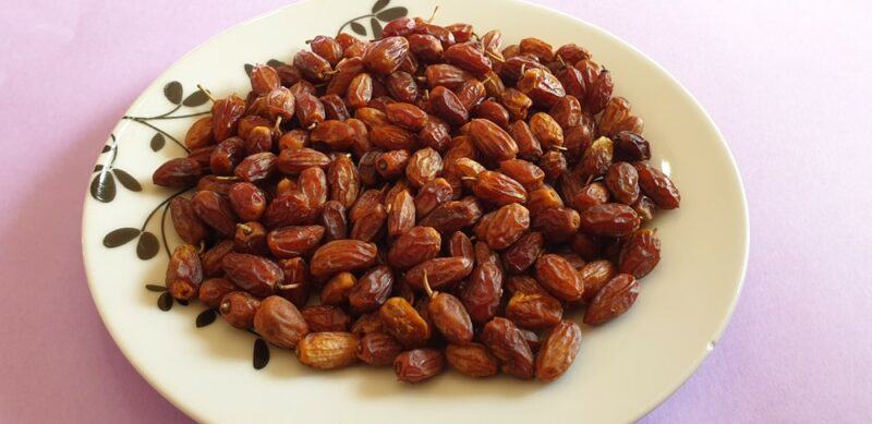 A wooden plate with dried nyii fruits on a pink table