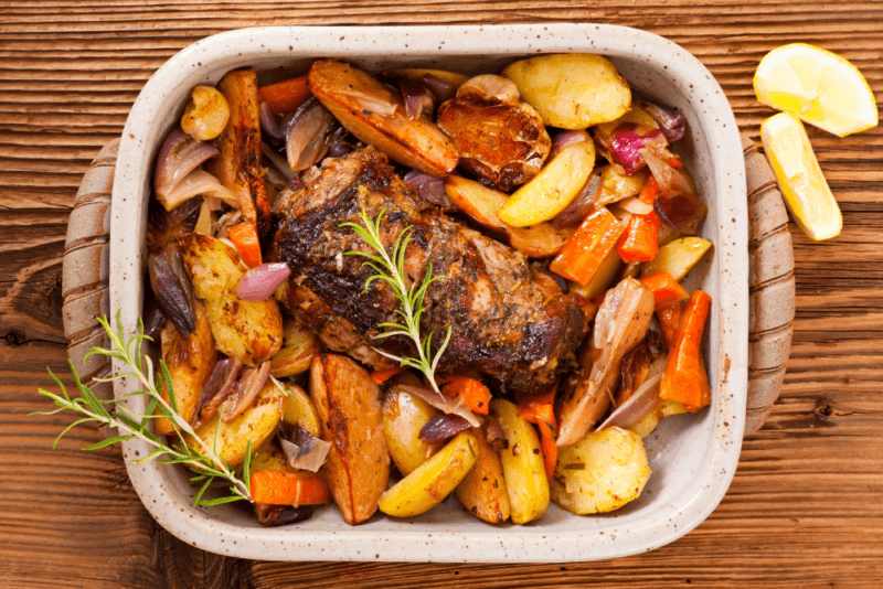 A large white tray of roast vegetables and lamb on a wooden table