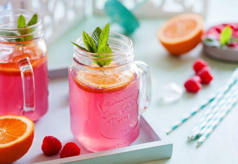 Mason jars filled with raspberry lemonade Crystal Light on a tray, with lemons and raspberries as well