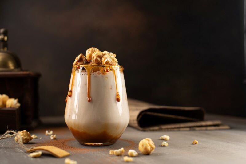 A tres leches cocktail with caramel and nuts as a garnish on a wooden table