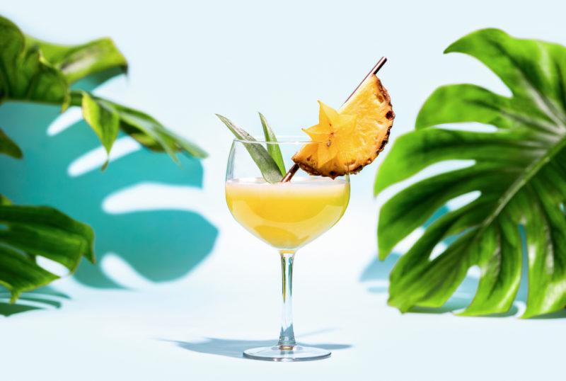 A tropical cocktail on a table garnished with pineapple and pineapple leaves