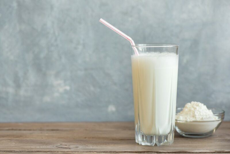 A tall glass filled with a vanilla protein shake, next to a small container of the protein powder