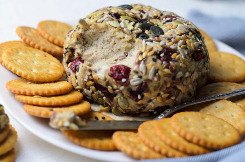 A white dish with a large vegan cheese ball and crackers