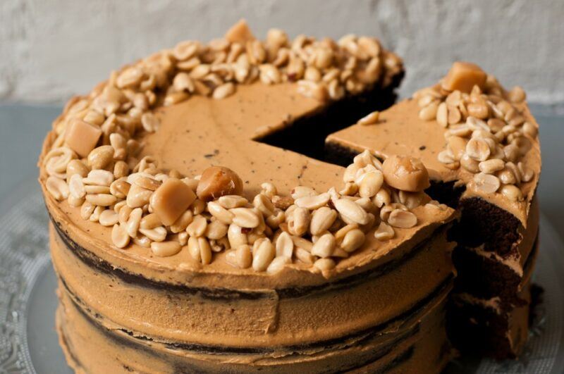 A vegan peanut butter and jelly cake that has been garnished with peanuts and has a slice partly cut out of it