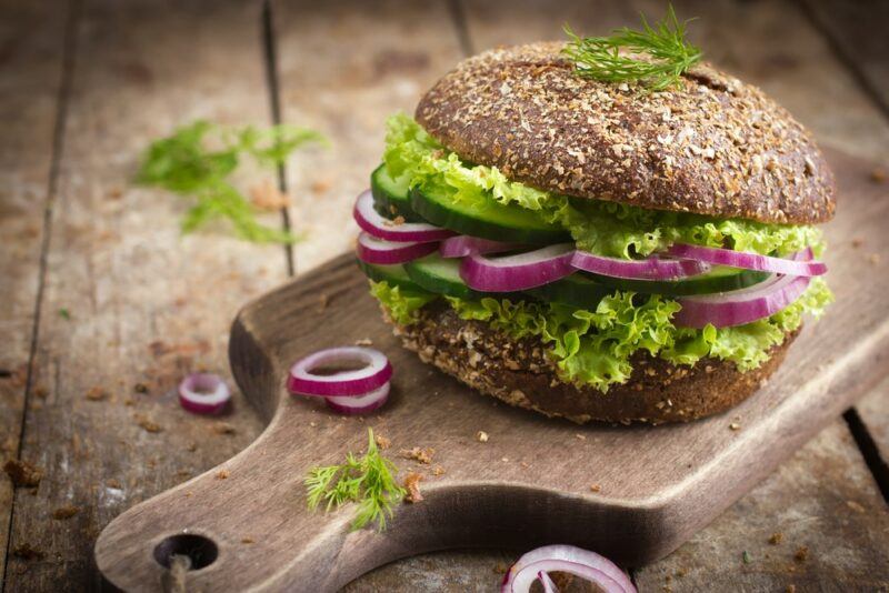 A wooden table and board, with a vegan burger on the board that's made using rye bread buns