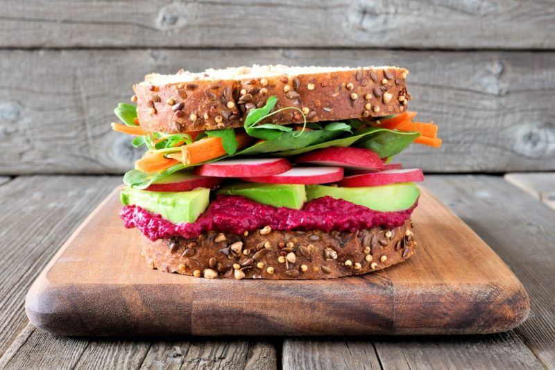 A vegan vegetable sandwich on a wooden board with fillings that include beetroot hummus and plenty of vegetables