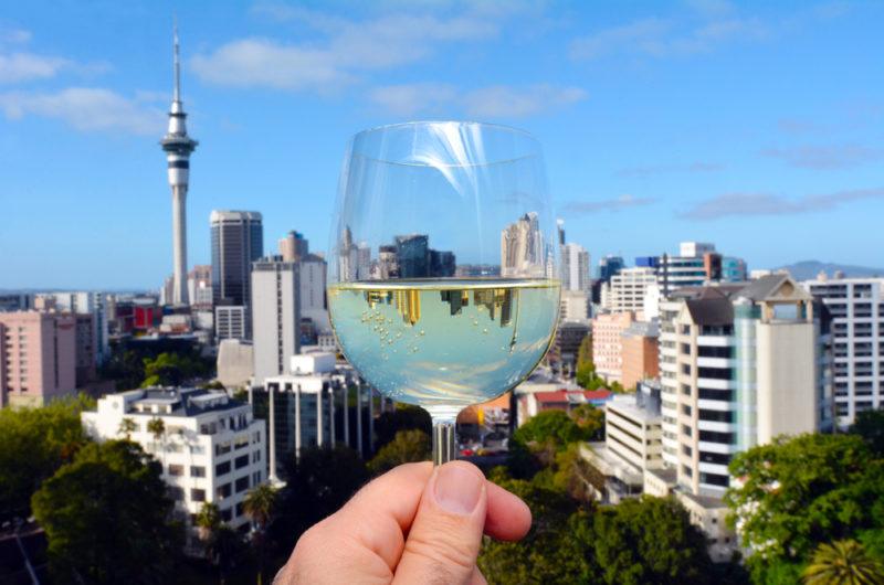 A glass of sauvignon blanc wine being held up against the Auckland skyline, with some of the skyline reflected in the wine