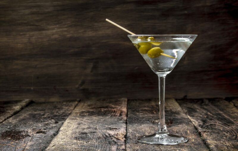 A vodka martini in a martini glass with two olives, on a wooden table