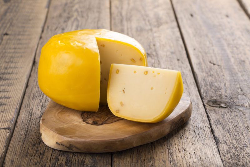 A wheel of gouda cheese with a wedge on a plate