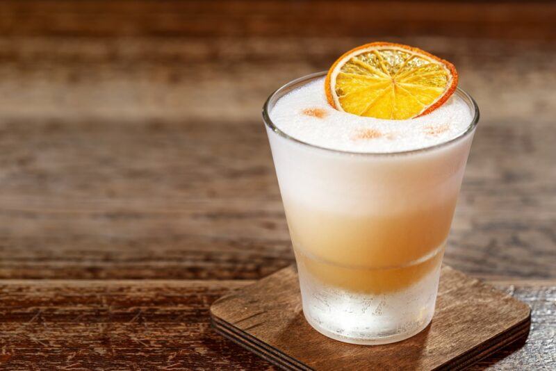 A wooden table with a coaster and a whiskey sour cocktail