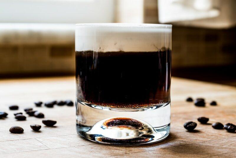 A layered white Russian cocktail on a table, surrounded by coffee beans